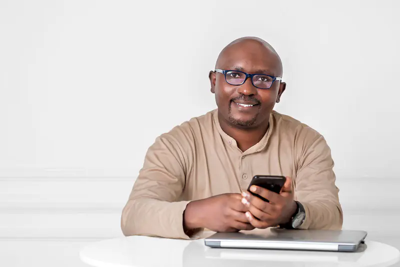 Entrepreneur souriant, son téléphone à la main, assis à une table devant un ordinateur portable