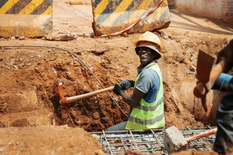 Ouvrier souriant, casque de chantier sur la tête, dans une tranchée en travaux