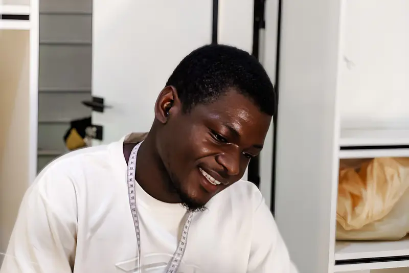 Tailleur souriant dans son atelier, un mètre ruban autour du cou